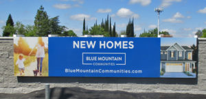Large blue banner installed on a sound-wall displaying the New Homes for sale.