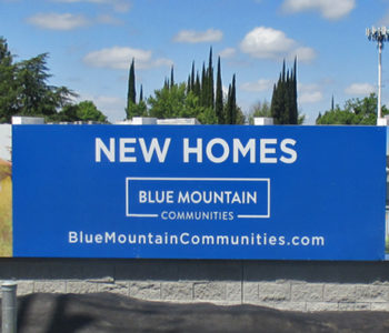 Large blue banner installed on a sound-wall displaying the New Homes for sale.