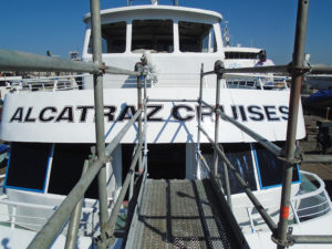 Walkway pointing towards the front of Cruise boat's 2nd floor. Visible is a large "Alcatraz Cruises" vinyl lettering applied to the front of the boat.