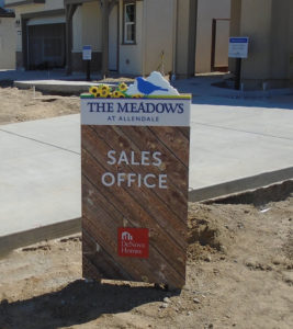 Sales Office sign for The Meadows at Allendale. Composed of faux wood planks background with a unique ID of yellow flowers and a blue bird on top of the sign.