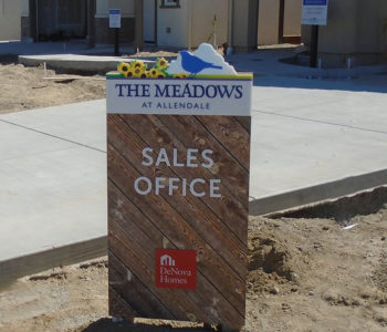 Sales Office sign for The Meadows at Allendale. Composed of faux wood planks background with a unique ID of yellow flowers and a blue bird on top of the sign.