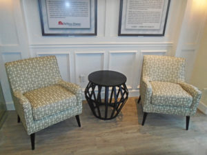 Client seating area composing of 2 brown arm chairs with geometric patterns and a black metallic end table.