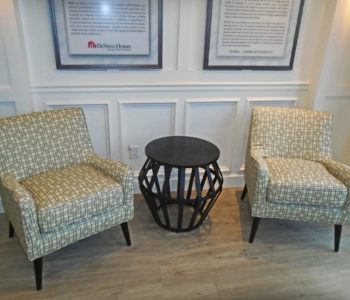 Client seating area composing of 2 brown arm chairs with geometric patterns and a black metallic end table.