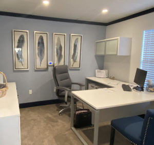 Interior sales office of Westfield displaying a workstation desk and 4 artwork frames featuring bird feathers.