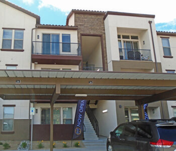 Small carport signs installed on outdoor carports, located in the foreground. Background is the apartment building and sandwiched in between is a banner flag staked into the ground with the Double R branding on it.