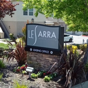 Grey and black Monument sign for LeSarra, with directional sign pointing to left.